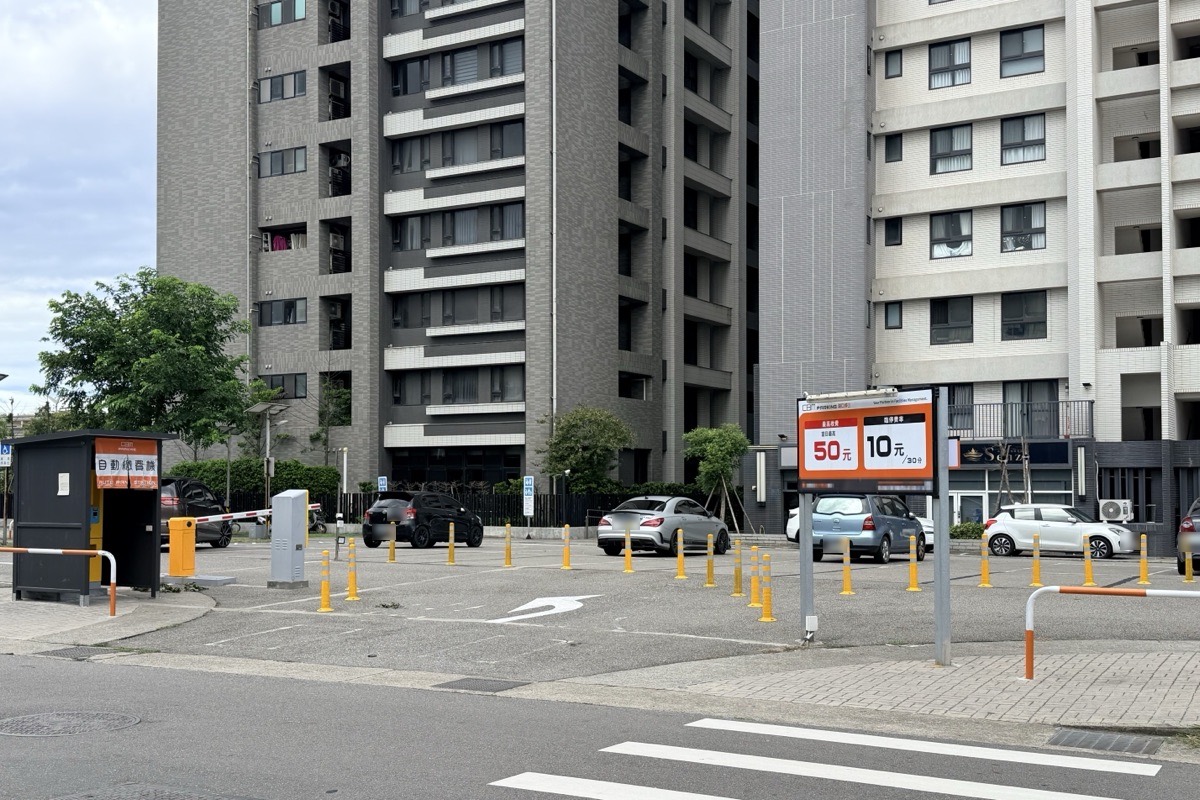 王爺壟停車場實景：診所大樓後方的平面停車場，可見出入口柵欄、自動繳費機與費率看板，後方為住宅大樓。